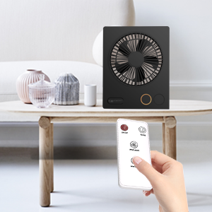 Compact black desk fan with remote control functionality, displayed on wooden table alongside decorative glass objects.