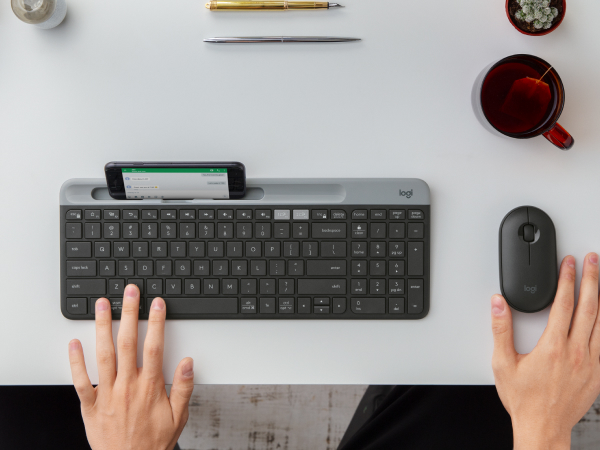 a man using k585 slim compact wireless graphite keyboard with phone holder and m350 cordless mouse