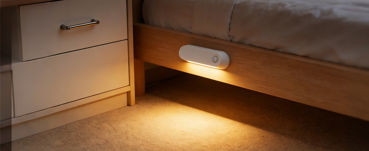 Motion sensor night light mounted near floor level, casting warm amber illumination along baseboards in dark setting.