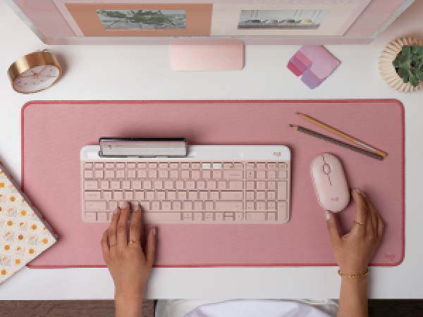 a woman using k585 slim compact wireless rose keyboard and m350 pebble shaped cordless pink mouse