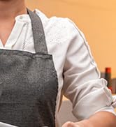 Partial view of a person wearing a gray apron over a white shirt, hands not visible. Image cropped to show torso only.
