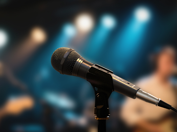 Professional microphone on stand against dark background with blue stage lighting creating dramatic atmosphere.