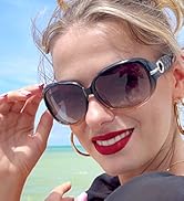 Large oversized sunglasses with dark lenses worn by a person with blonde hair. Beach or ocean scene visible in the background.
