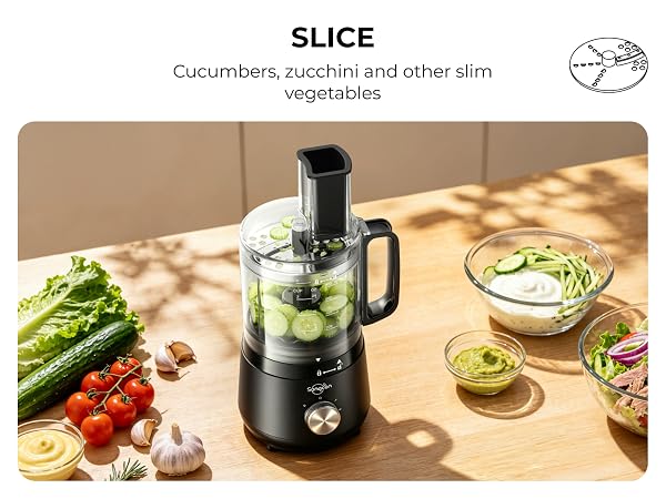 Mini food processor slicing cucumbers beside fresh produce, dips and a prepared salad