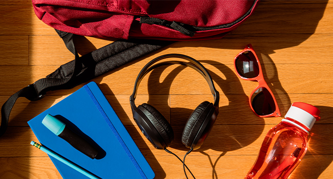 Panasonic RP-HT161 headphones scattered on wood floor with a backpack, a notebook and a pencil.