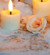 Lit white pillar candles arranged with pale pink roses on a textured surface, creating a soft, romantic atmosphere.