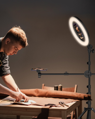 Desk setup with an adjustable ring light mounted on an articulating arm, illuminating a workspace where craftwork is being performed.