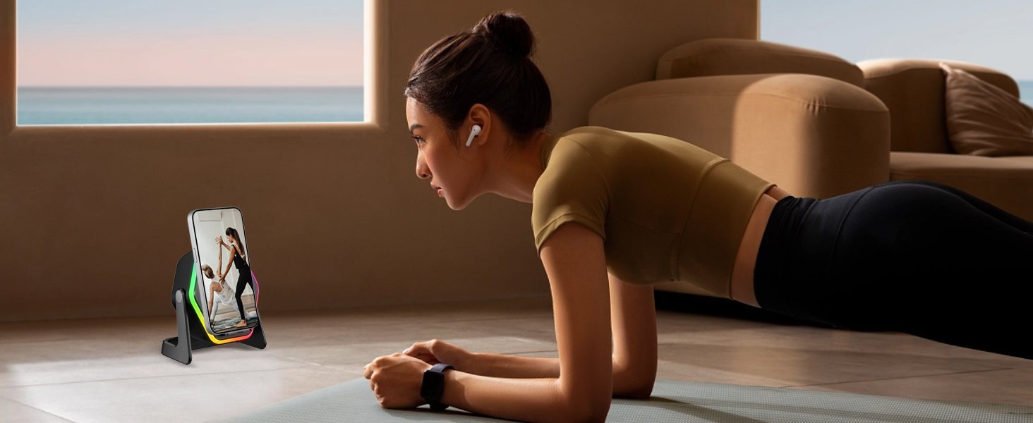 Person in plank position on wooden floor doing exercise while viewing device propped in stand against brown couch.