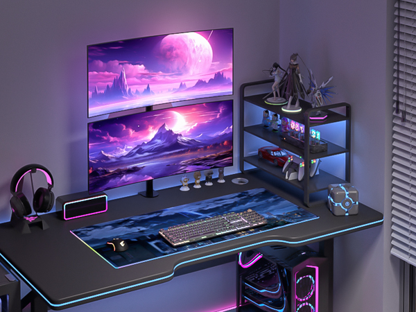 Gaming setup with large monitor displaying purple cosmic scenery, RGB-lit desk, gaming keyboard, mouse pad, headphone stand, and tiered peripheral shelf.
