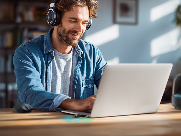 Man Wearing Headphones Using Laptop with USB WiFi and Bluetooth Adapter Plugged in