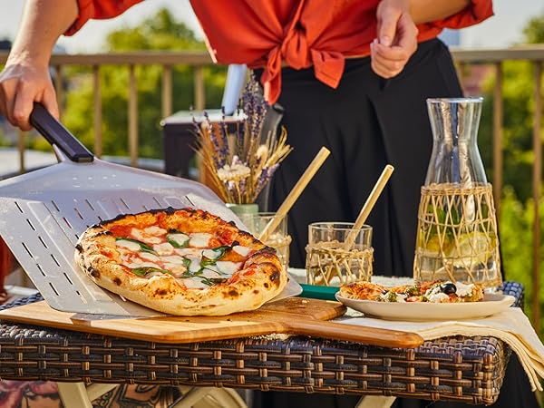 Outdoor pizza dining scene with hands serving a freshly baked pizza, alongside glasses and a carafe of water.