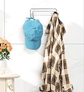 Wall-mounted coat rack with light blue baseball cap and patterned beige blanket hanging from hooks. Small plant in orange pot visible on left side.