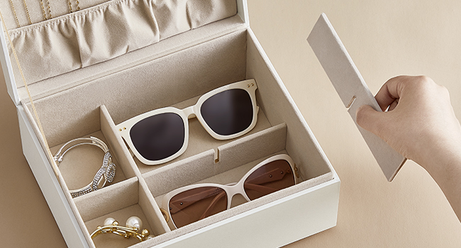 Beige storage box with compartments for sunglasses and jewelry. Two pairs of sunglasses and accessories visible inside.