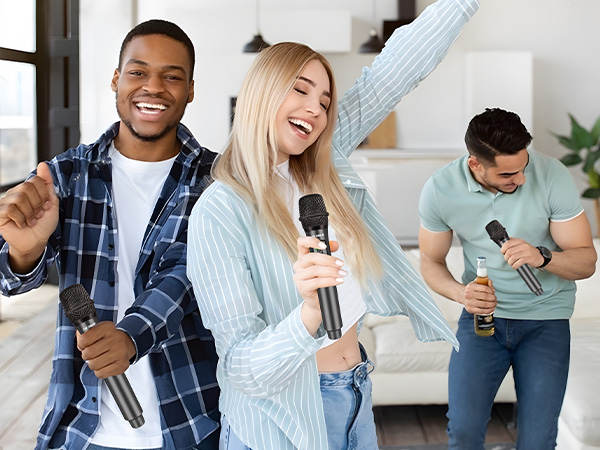 Three people singing karaoke indoors, each holding wireless microphones. They appear enthusiastic and joyful while performing in a home setting.