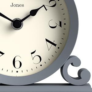 Jones wall clock detail showing elegant black numerals and hands against cream-colored face, with decorative grey scroll detail.