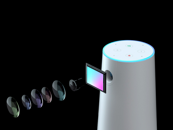 White cylindrical smart speaker with blue light ring on top. Side display shows colorful interface. Multiple ear-shaped devices in various colors displayed in foreground.