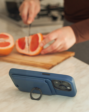 Blue smartphone case with built-in ring holder and kickstand, displayed on a wooden cutting board next to sliced grapefruit.
