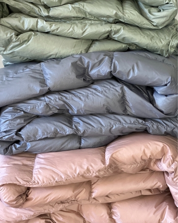 Stack of green, blue and pink Noora North ultralight down camping blankets, perfect for backpacking