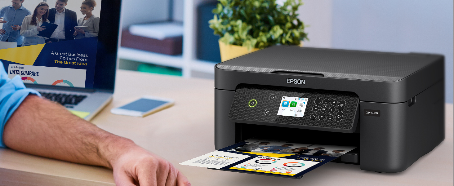 Black Expression Home XP-4200 printer sitting on desk with colorful business flyer in output tray.