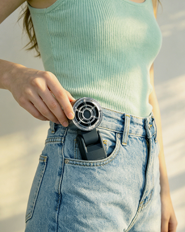 Analog wristwatch with dark dial and silver bezel worn in jean pocket of person in light blue ribbed top. Watch features round face with visible hands and markers.