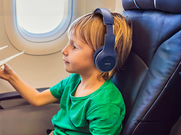 Wireless over-ear headphones in navy blue worn by a child on an airplane. Headphones feature a padded headband and ear cups for comfort during travel.