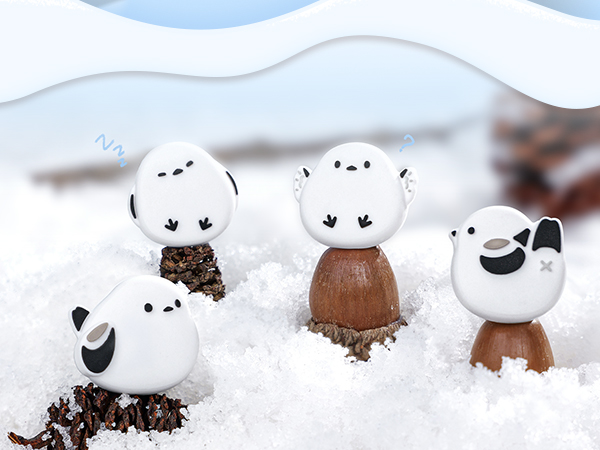 Decorative snow scene featuring three white figurines shaped like round characters sitting in artificial snow.