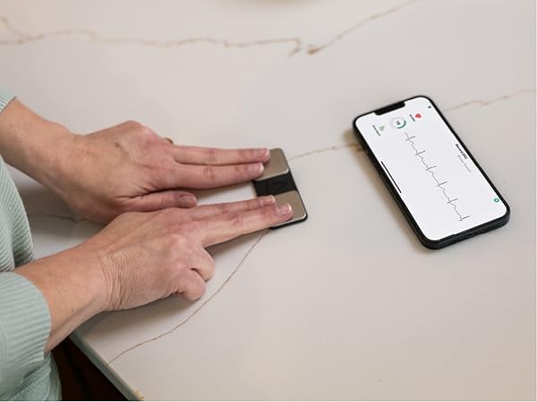Person taking EKG with KardiaMobile device and phone screen showing EKG recording.