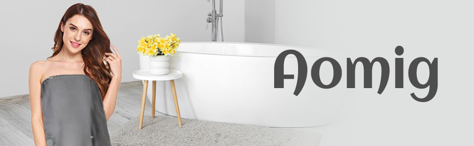 Modern bathroom setting featuring a freestanding white bathtub, small wooden side table with yellow flowers, and grey text reading 'Aomig'.