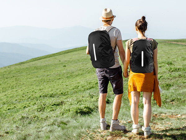 Two hikers with backpacks walking on a grassy hill overlooking a scenic landscape. One wears yellow shorts, the other black shorts.
