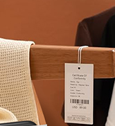 Close-up of a fabric tag attached to furniture, likely a care or product information label. Partial view of textured upholstery visible.