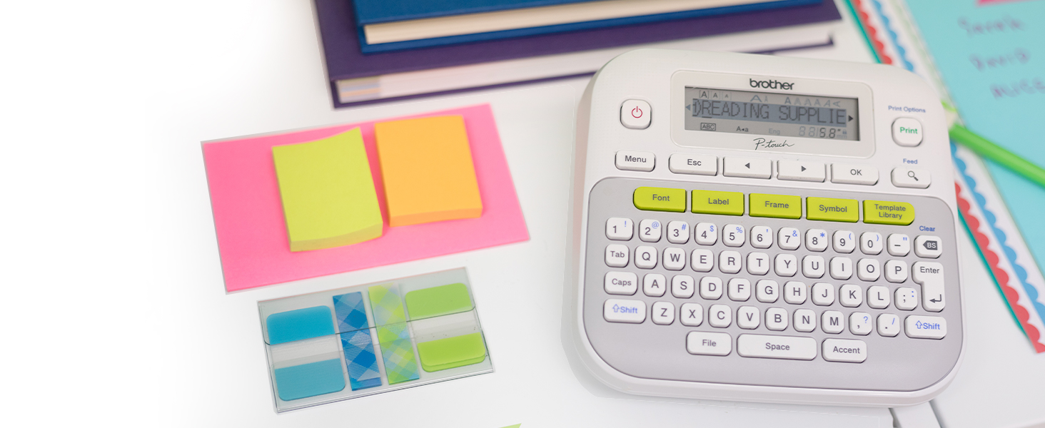 Brother P-touch PTD210SV Label Maker on desk with notebooks, papers. Screen reads READING SUPPLIES