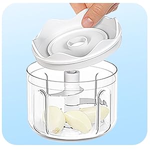 Clear manual food chopper with white lid showing spiral blade mechanism inside. Container holds chopped light-colored ingredients.