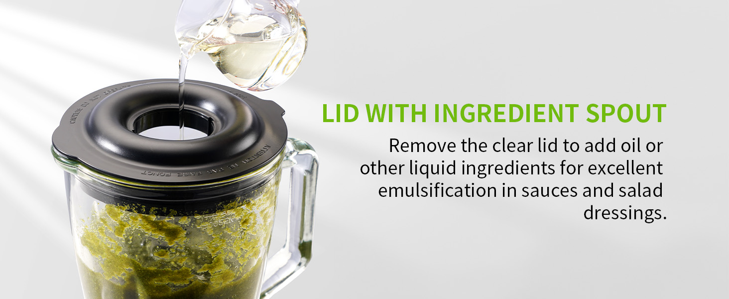 Kitchen appliance with clear lid and ingredient spout. Black rim on glass container holding green mixture. Text explains lid removal for adding liquids to sauces and dressings.