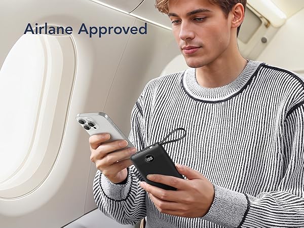 A striped sweater-wearing passenger using a mobile device and power bank while seated by an airplane window marked 'Airplane Approved'