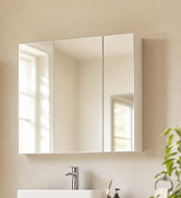 Bright interior bathroom space with white framed mirror above beige vanity cabinet, white walls, and natural lighting from window.