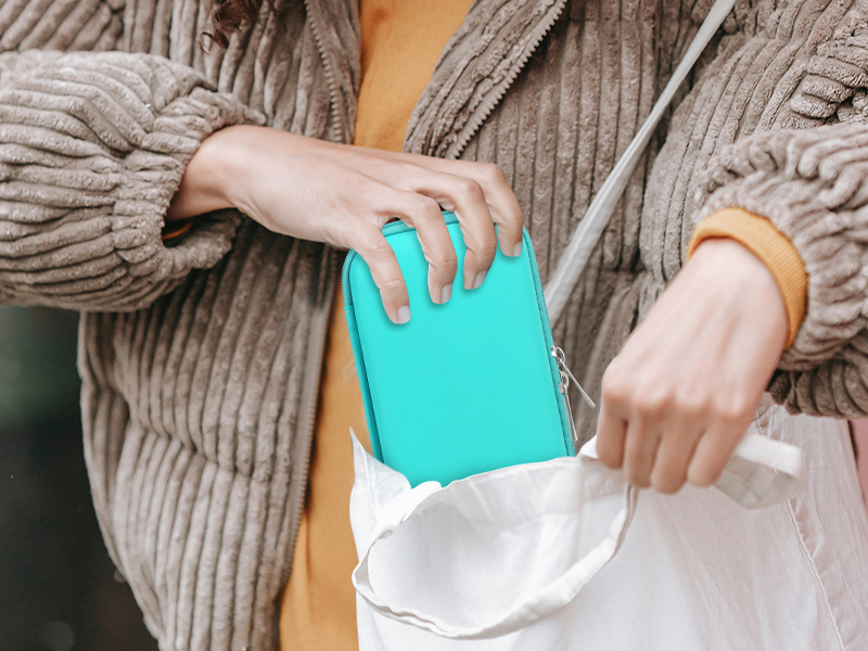 Hands in gray sweater sleeves inserting a turquoise-colored item into a white bag or container.