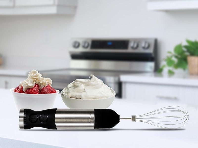 Hand blender with whisk on a white counter in front of two bowls of strawberries and whipped cream