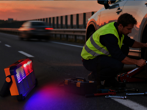 Driver changing tire on roadside at sunset with SOS strobe work light flashing red blue