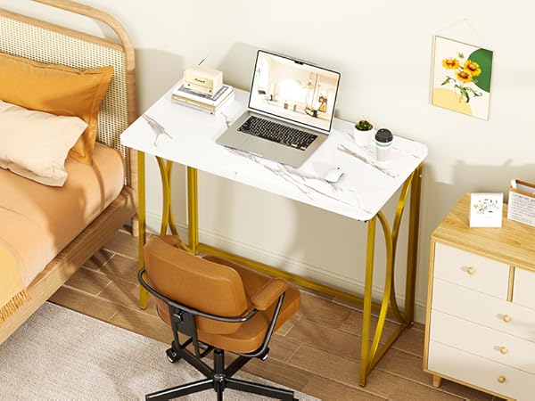 A bedroom with a bed, folding table, chair, a painting above the table and a cabinet
