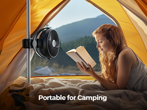 Portable camping fan mounted inside a tent. A person reads a book on a sleeping bag with mountains visible through the tent opening.