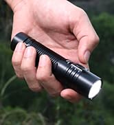 Hand holding a black cylindrical device or tool against an outdoor background.