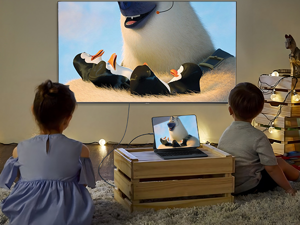 Home theater setup showing projected movie on wall, laptop on wooden crate, and cozy floor seating arrangement with cushions.