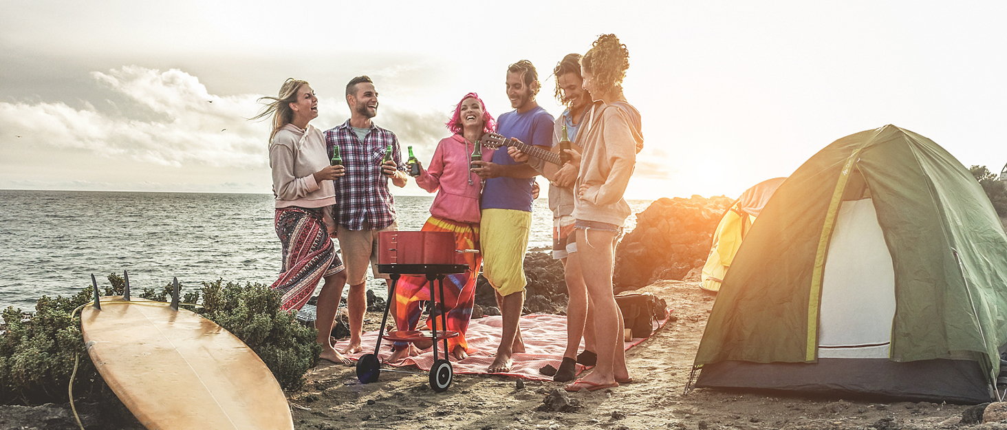 a group of people standing around a grill on a beach.