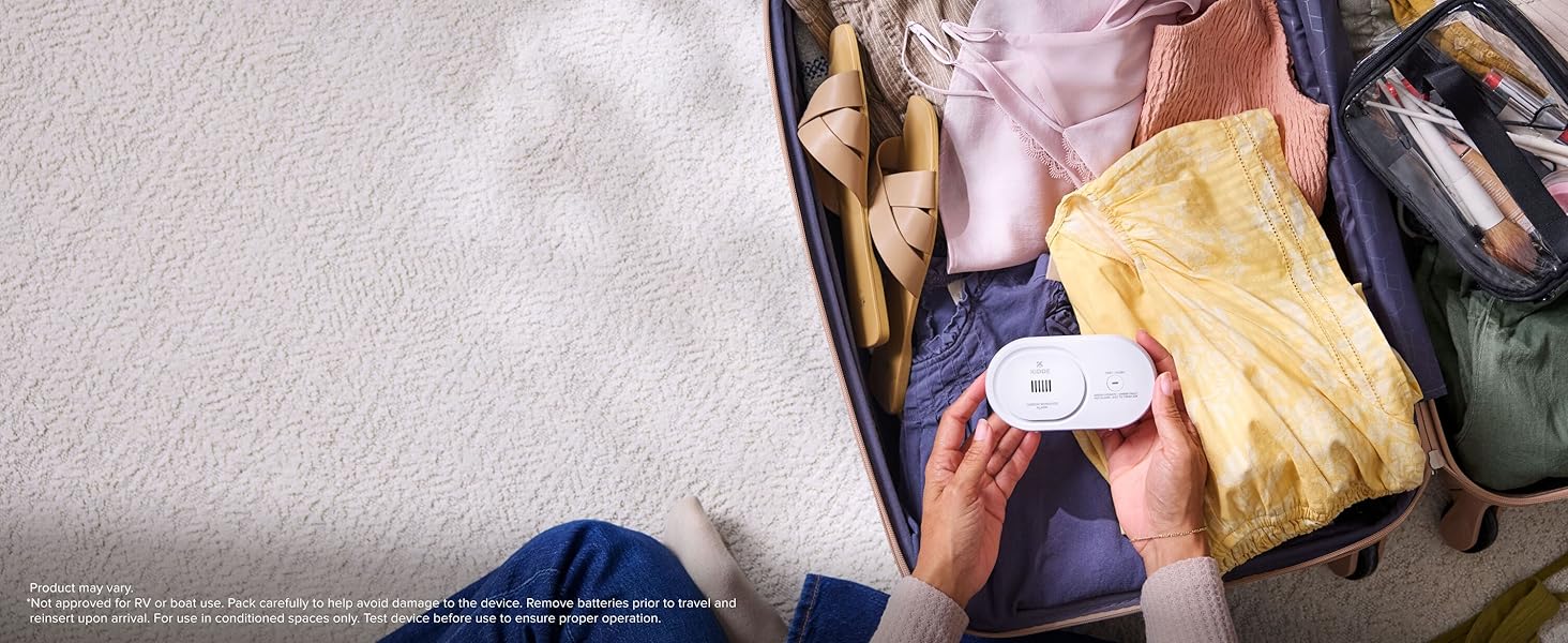 Kidde AA battery CO detector being packed in a suitcase for travel safety, desktop image