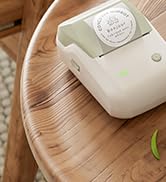 Beige wireless earbud case on a wooden surface. Compact, rounded square shape with a subtle brand logo visible.