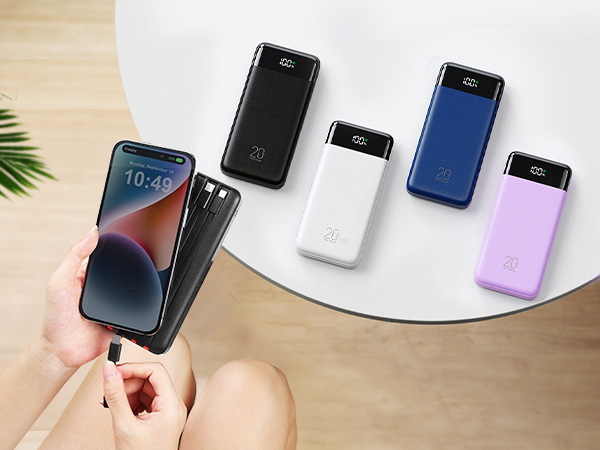 Hand holding smartphone with display showing time 10:45. Collection of five portable power banks in black, white, blue, and purple arranged on white circular surface with plant leaf visible.