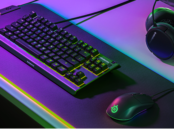 - A SteelSeries desk setup with Apex keyboard, Rival 3 mouse, Arctis headset, and QcK Prism mousepad