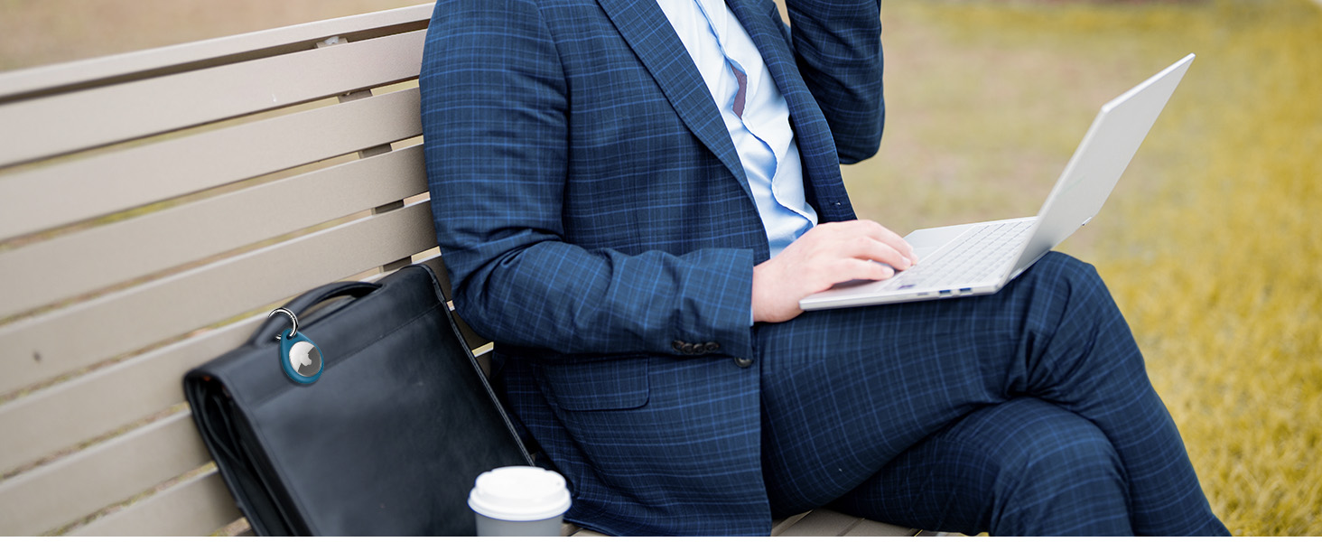 Person in business attire sitting outdoors, using a laptop computer on their lap. Only torso and legs visible.