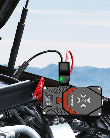 Portable jump starter with wireless charging pad mounted in a vehicle. Device features a digital display, red accents, and is connected to a battery with jumper cables.
