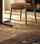 Wooden chair with natural finish and woven seat displayed on wooden flooring with warm lighting.